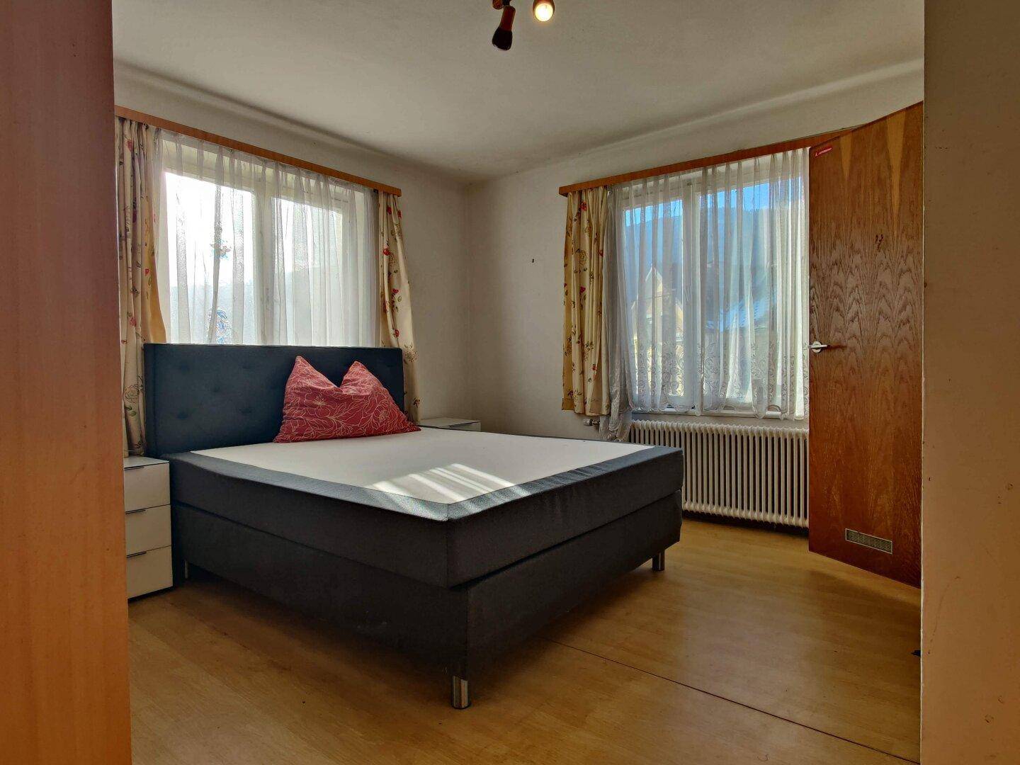 Schlafzimmer mit Doppelbett, Holzboden und großen Fenstern für viel Tageslicht.