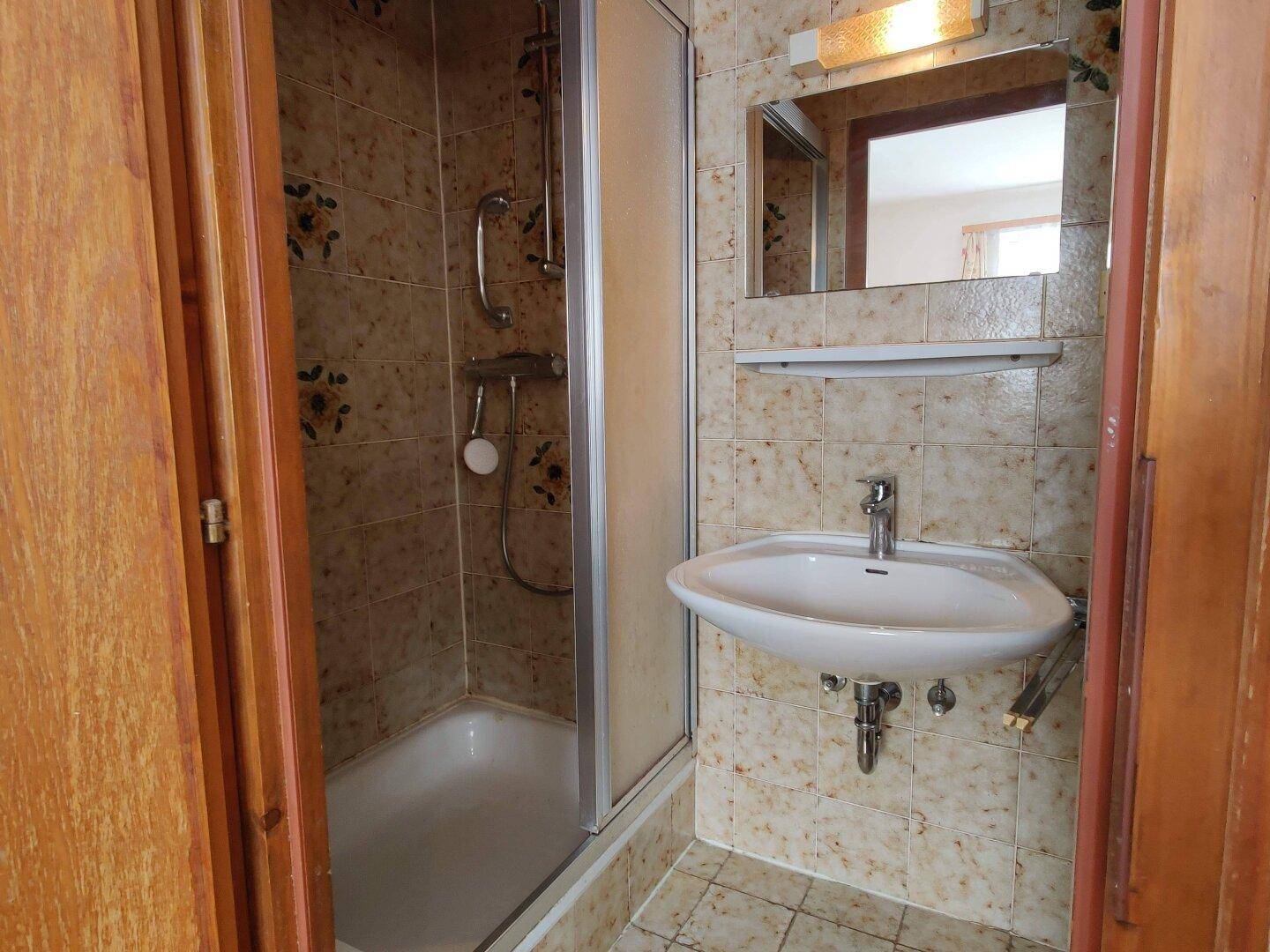 Kleines Badezimmer mit Duschkabine, Waschbecken und beigen Fliesen.
