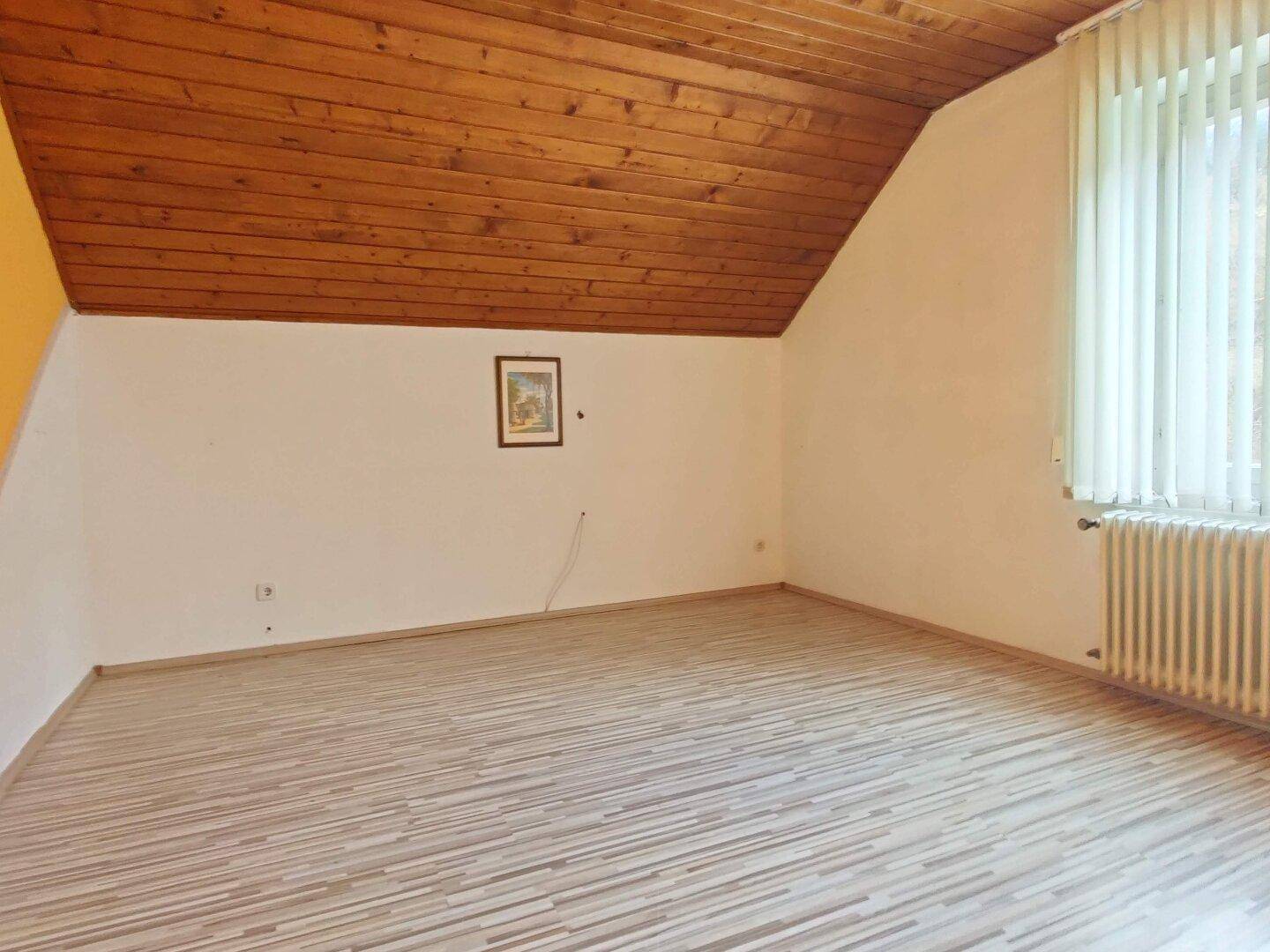 Helles Zimmer im Dachgeschoss mit Holzdecke und Laminatboden.
