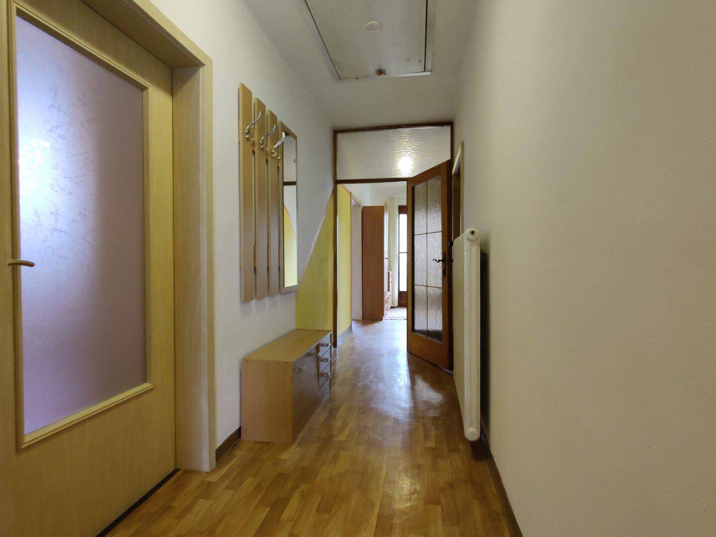 Langer Flur mit Holzboden und Garderobe, der zu weiteren Räumen führt.