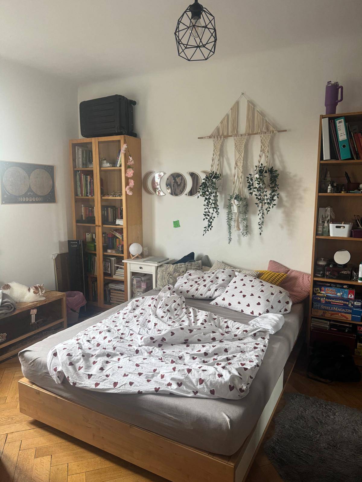 Schlafzimmer mit Holzbett, Bücherregalen und dekorativen Elementen, bietet eine persönliche und helle Atmosphäre.