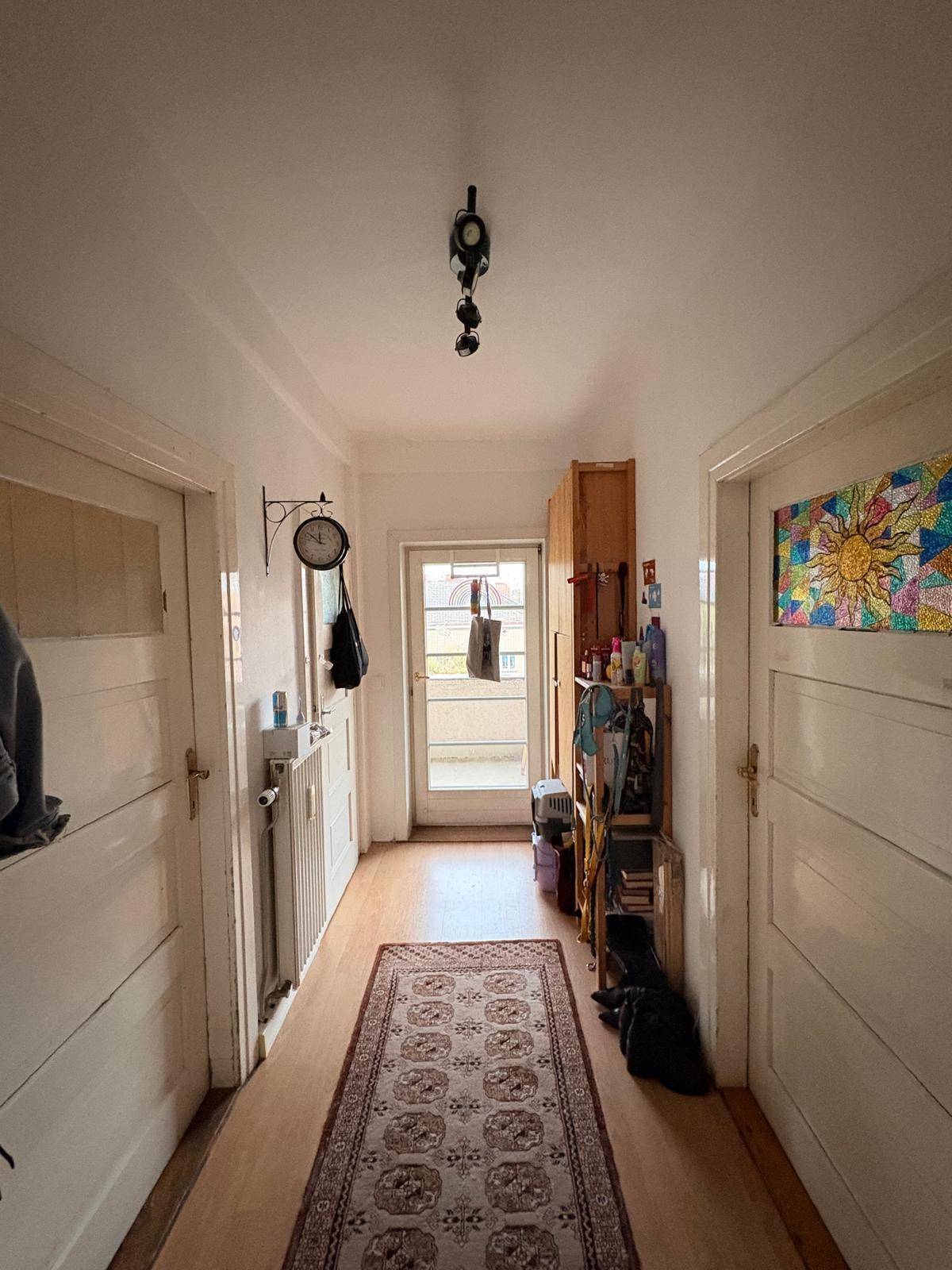 Heller Flur mit Holzfußboden und Teppich, führt zu verschiedenen Räumen und einem kleinen Balkon.