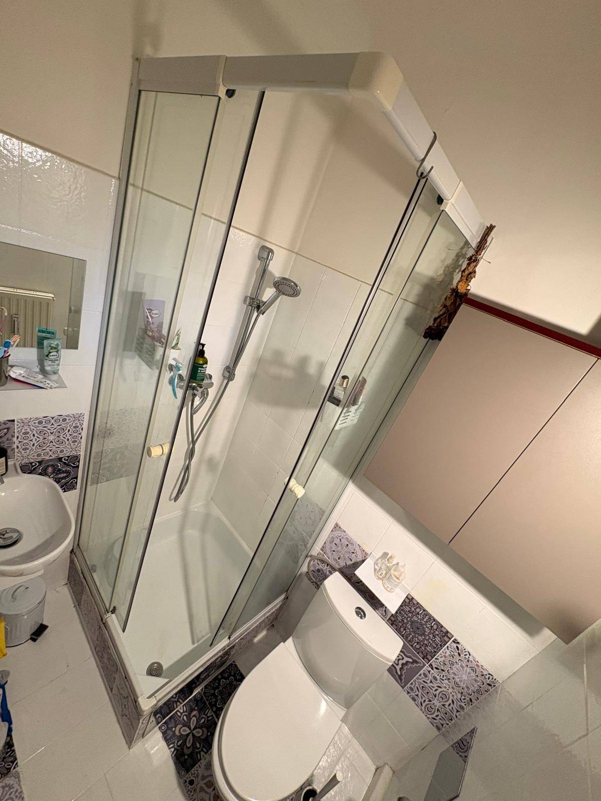 Badezimmer mit Duschkabine, Toilette und kleinem Waschbecken, verziert mit gemusterten Fliesen.