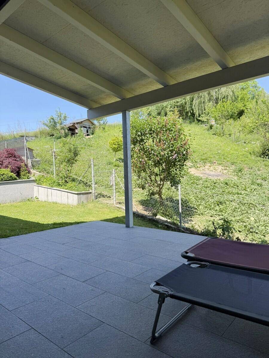 Überdachte Terrasse mit Liegestühlen und weitem Blick auf den grünen Gartenhang.