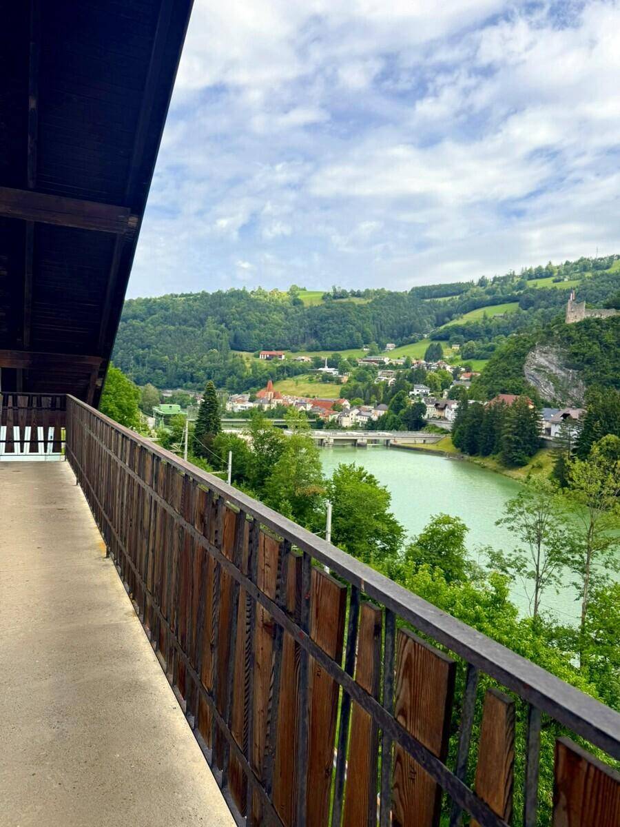 Langer Balkon mit Holzgeländer und weitem Blick auf den See und die umliegende Landschaft.