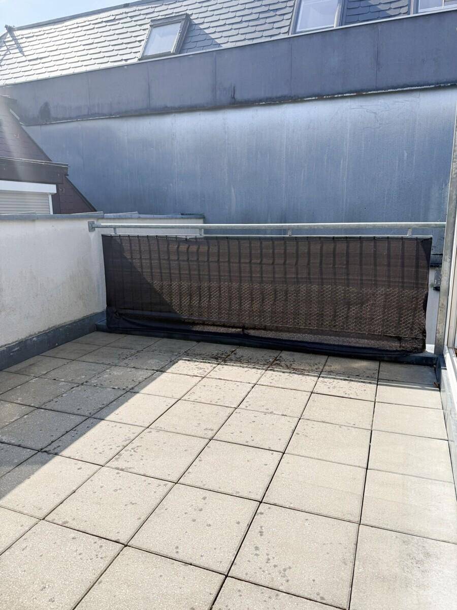 Sonnenterrasse mit grauen Fliesen und Sichtschutz, umgeben von Dächern.