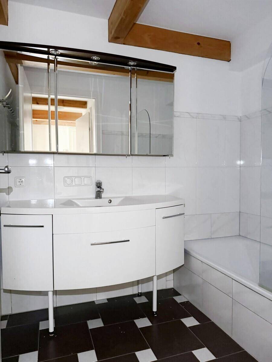 Badezimmer mit weißem Waschtisch, Spiegelschrank, Badewanne und gemustertem Fliesenboden.