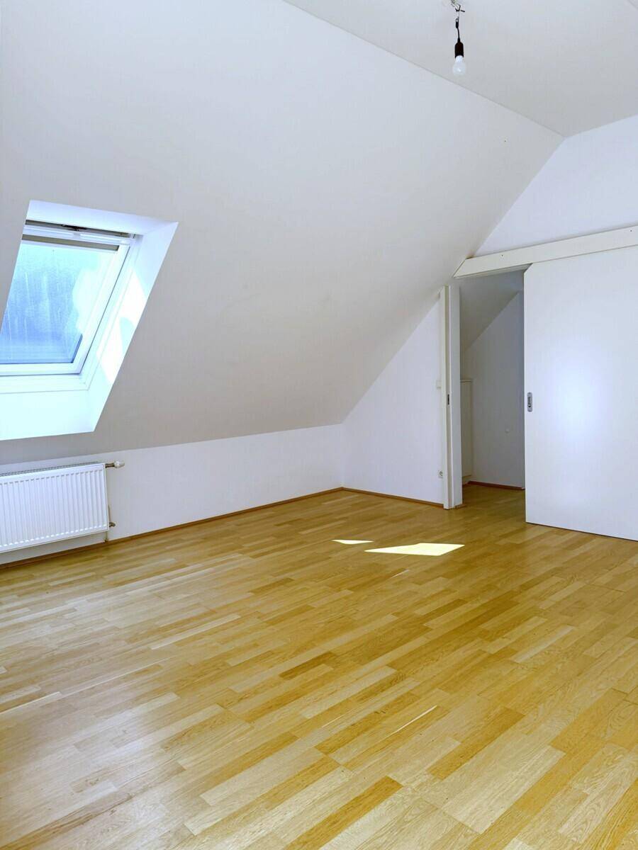 Geräumiges Dachzimmer mit hellem Holzboden, Dachfenster und praktischer Schiebetür.