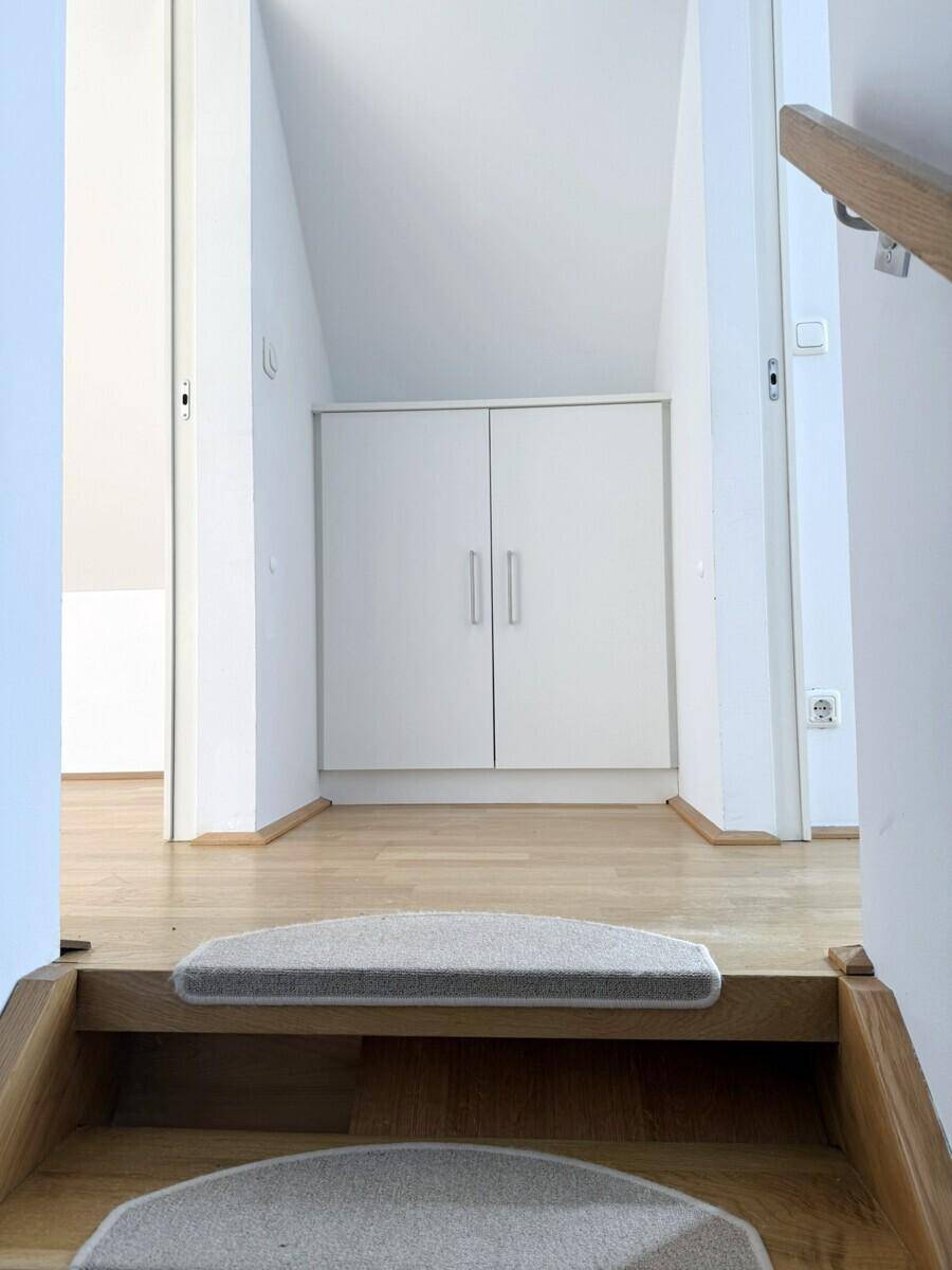 Treppenaufgang mit hellem Holz und integriertem weißen Schrank auf dem oberen Treppenabsatz.