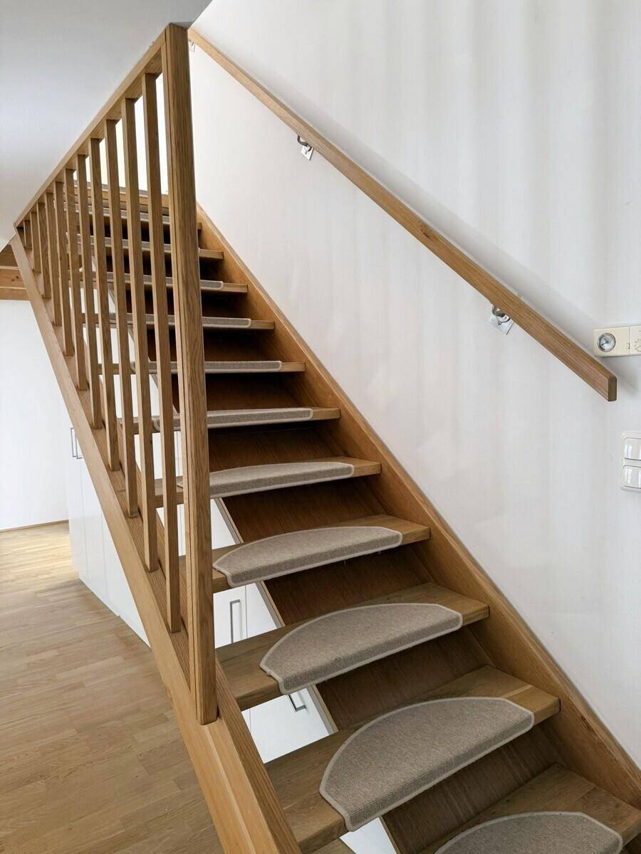 Detailansicht einer Holztreppe mit Teppichstufen und passendem Holzgeländer.