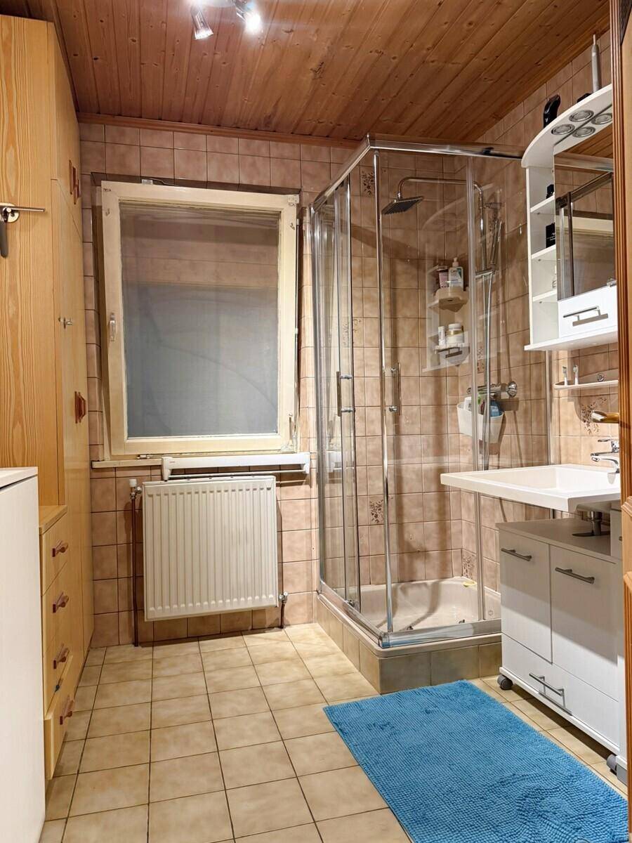 Badezimmer mit Duschkabine, Waschbecken und Holzdecke, in warmen Farbtönen gehalten.