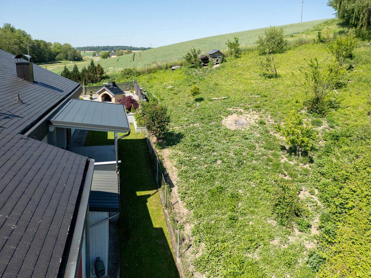 Seitenansicht des Hauses mit angrenzendem grünen Hügel und ländlicher Umgebung.