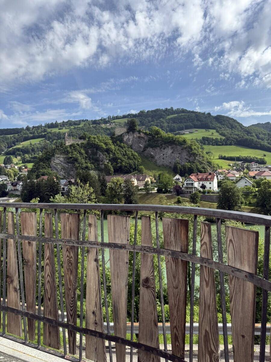 Panoramablick von einem Balkon auf eine malerische Landschaft mit grünen Hügeln und einer Burgruine.