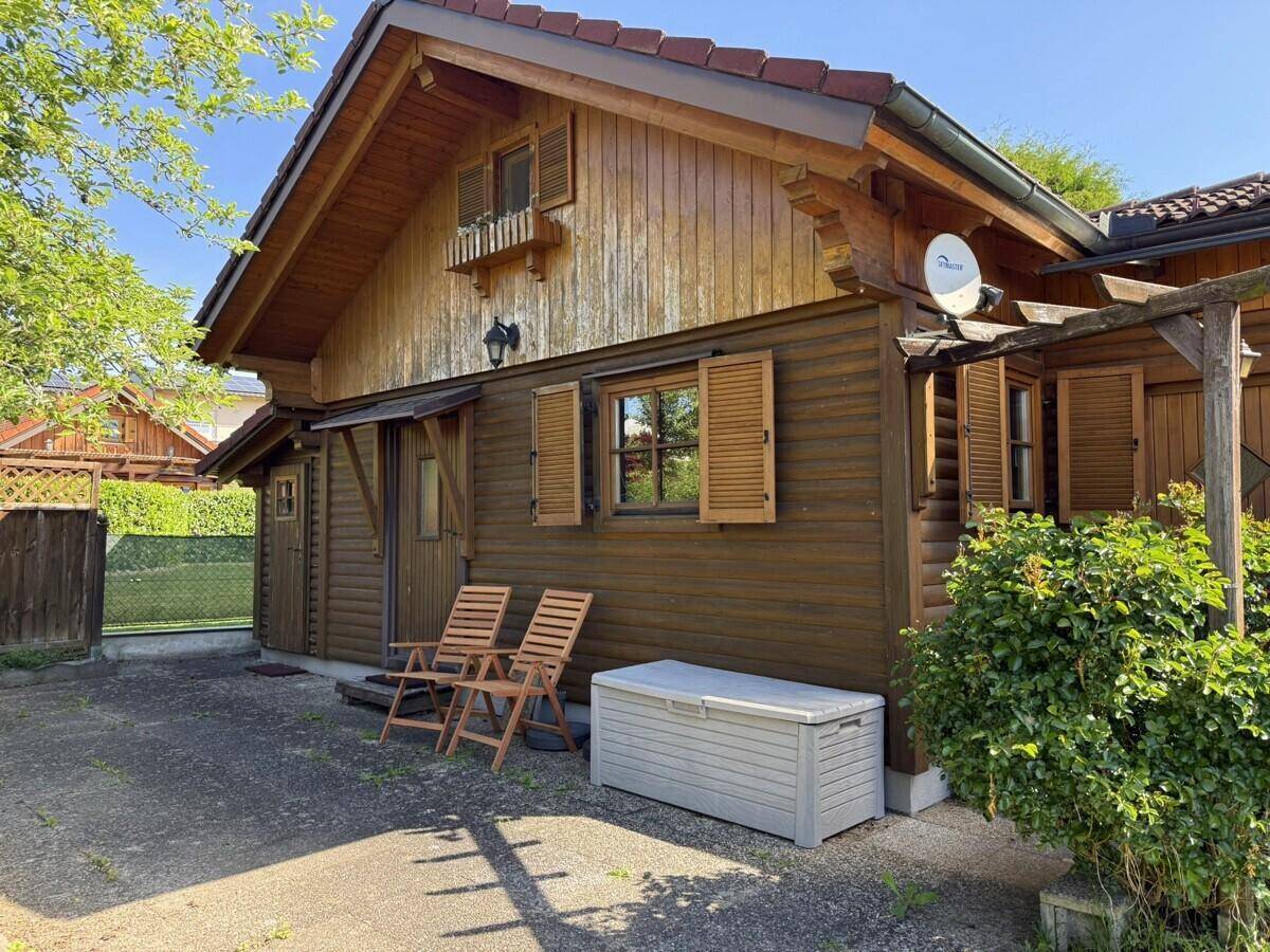 Rustikale Holzhausfassade mit Fensterläden und kleinem Eingangsbereich, umgeben von Bäumen.