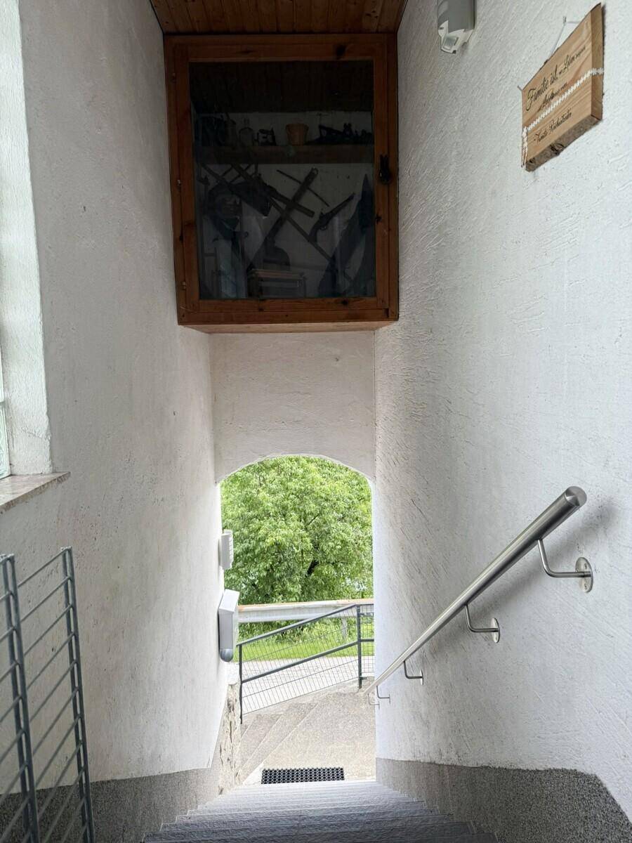 Treppenhaus mit weiß gestrichenen Wänden und Blick ins Grüne durch einen Bogen.