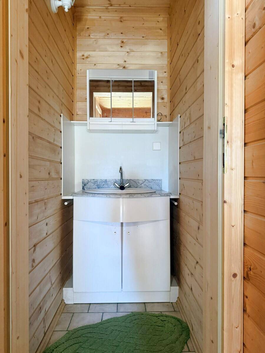 Kleines Badezimmer oder Gäste-WC mit Holzvertäfelung, Waschbecken und einem Spiegel über dem Waschtisch.