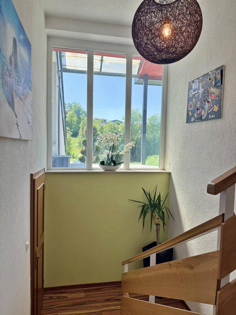 Heller Treppenaufgang mit Holzstufen und großem Fenster mit Blick ins Grüne.