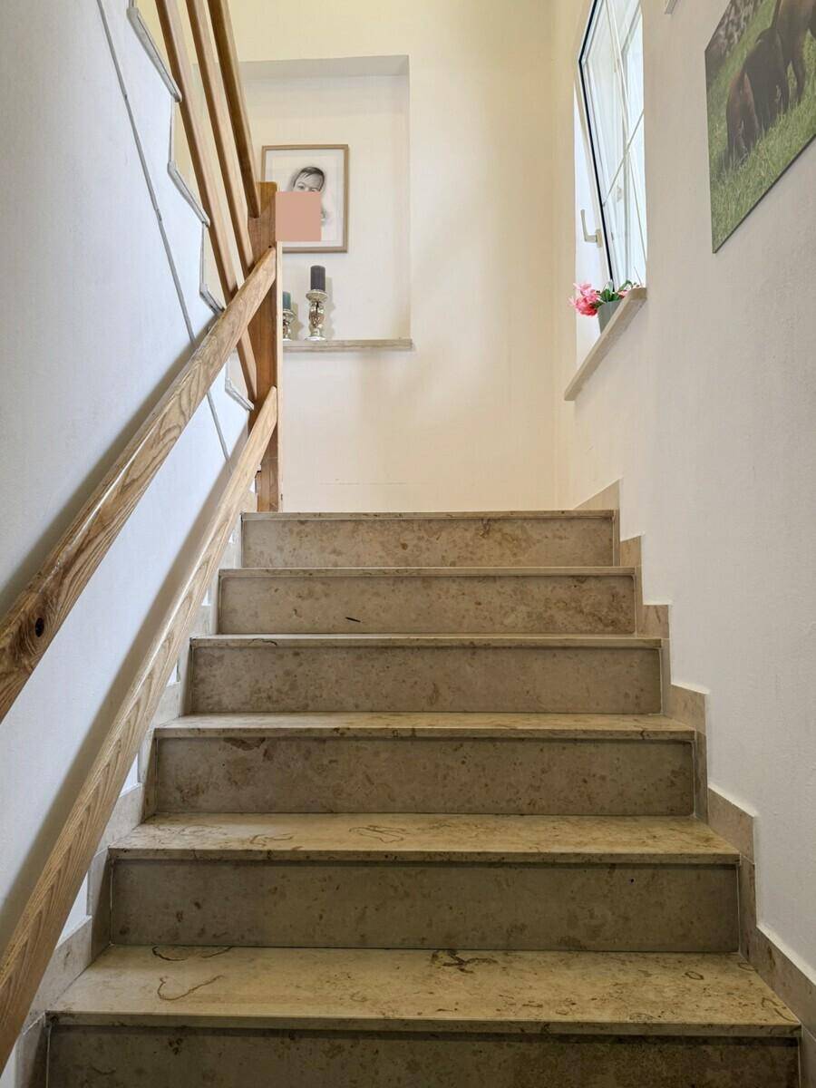 Treppenhaus mit Steinstufen und Holzgeländer, das zu den oberen Etagen führt.