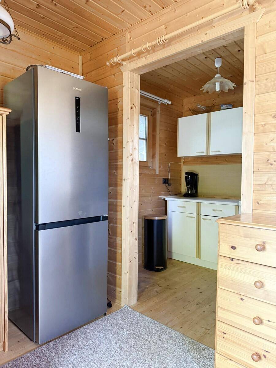Kleiner Küchenbereich mit Holzvertäfelung, einem modernen Kühlschrank und weißen Schränken.