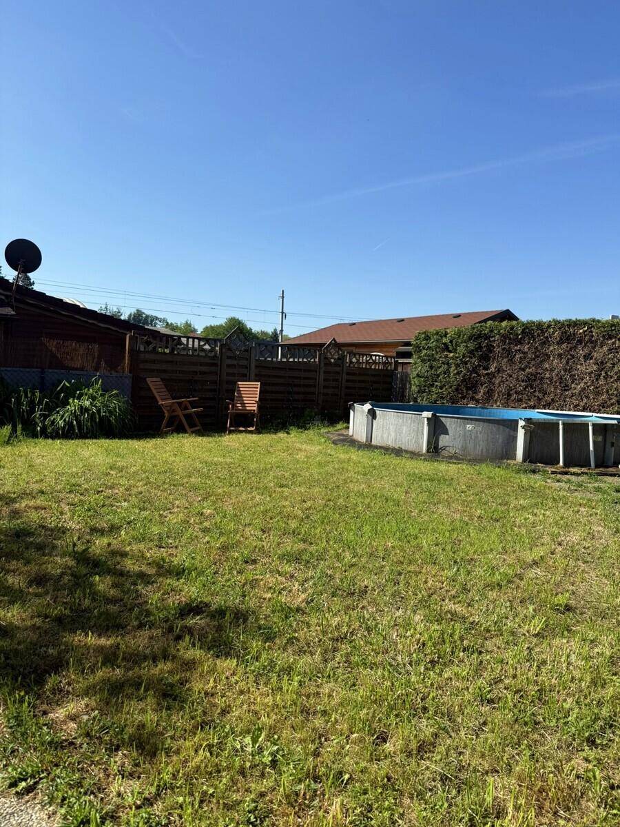 Weitläufiger Garten mit Aufstellpool, Rasen und einer dichten Hecke im Hintergrund an einem sonnigen Tag.