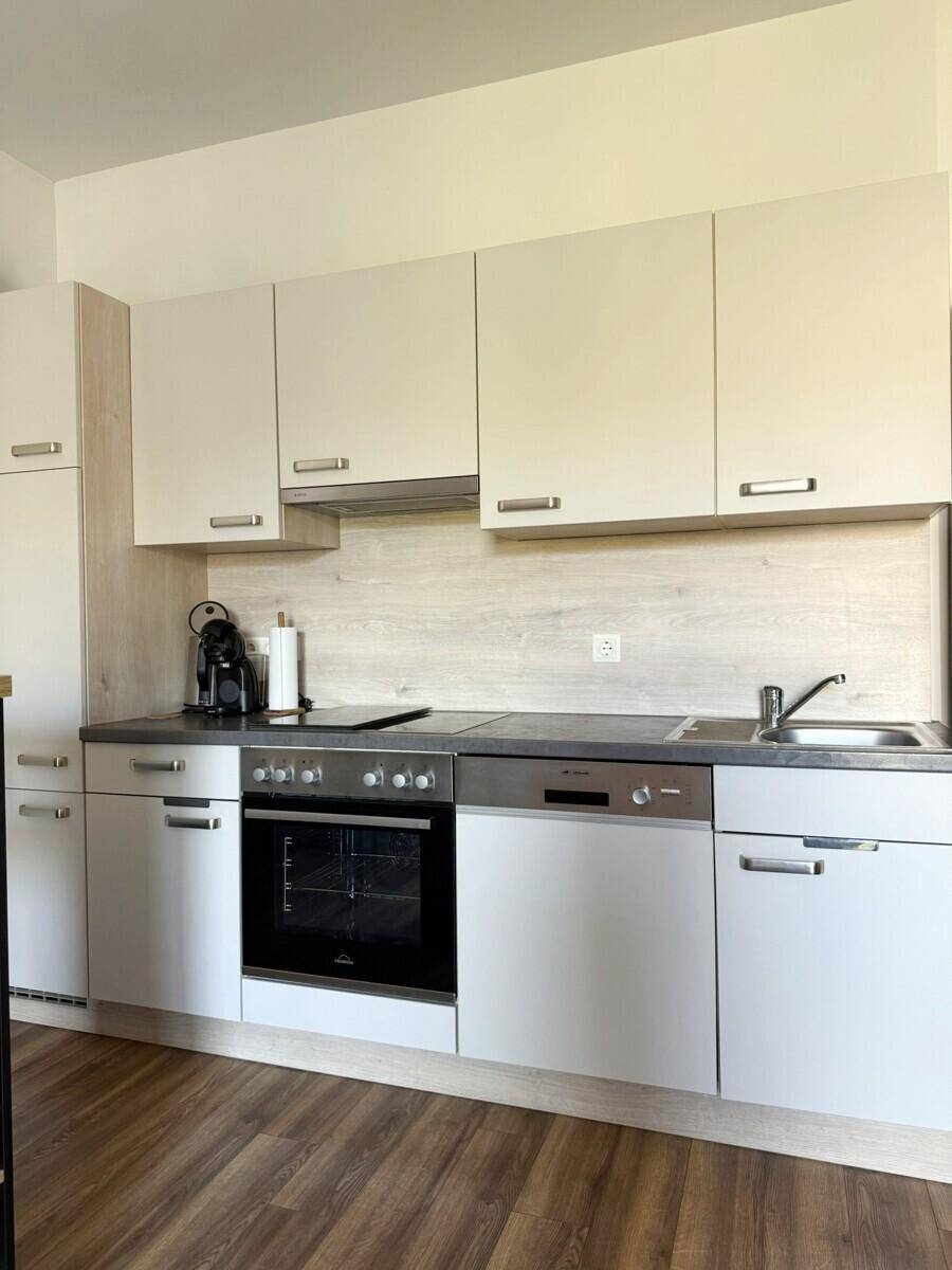 Moderne Einbauküche mit hellen Schränken, integrierten Geräten und Laminatboden.