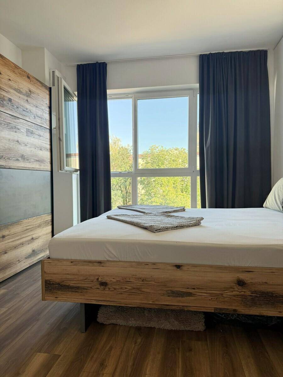 Schlafzimmer mit Holzbett, Laminatboden und großem Fenster mit Vorhängen.