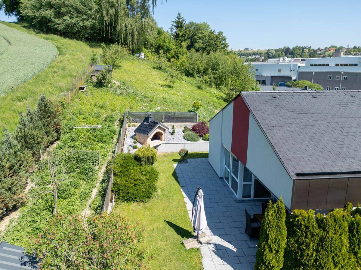 Gartenbereich mit gepflasterter Terrasse, Sonnenschirm und Außen-Pizzaofen.