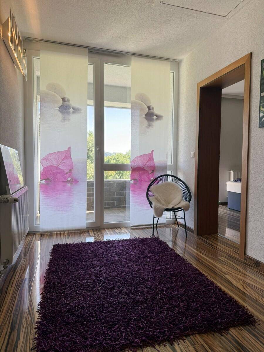Heller Flur mit gemustertem Holzboden, lila Teppich und Zugang zum Balkon.