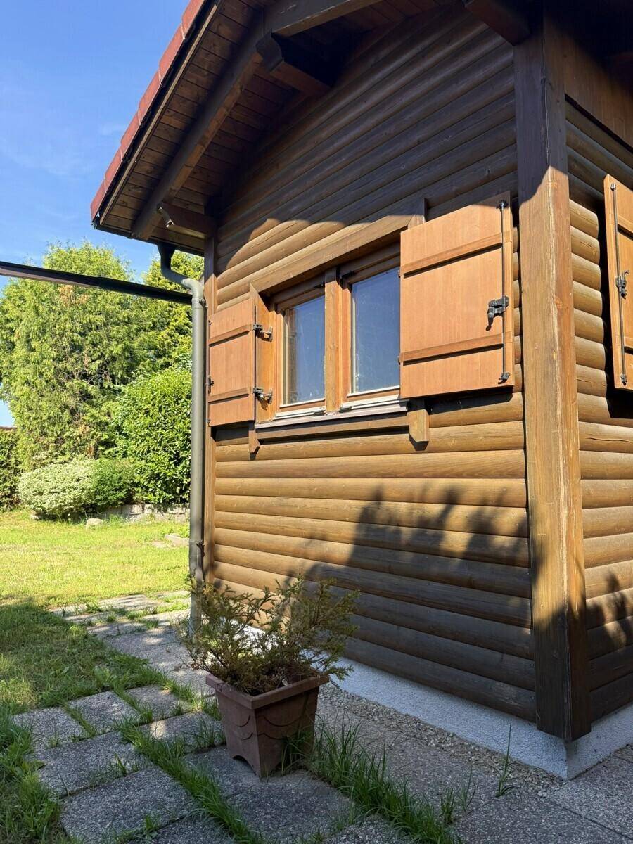 Nahaufnahme der Holzfassade eines Hauses mit geschlossenen Fensterläden und Blick ins Grüne.