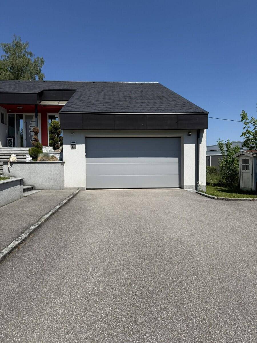 Moderne Garage mit Sektionaltor und breiter Zufahrt zum Einfamilienhaus.