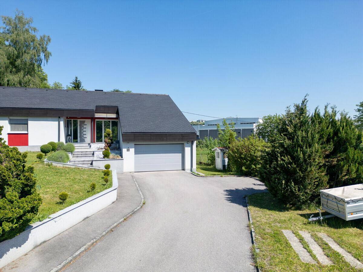 Haus mit Garage, langer Auffahrt und umgebender grüner Landschaft.