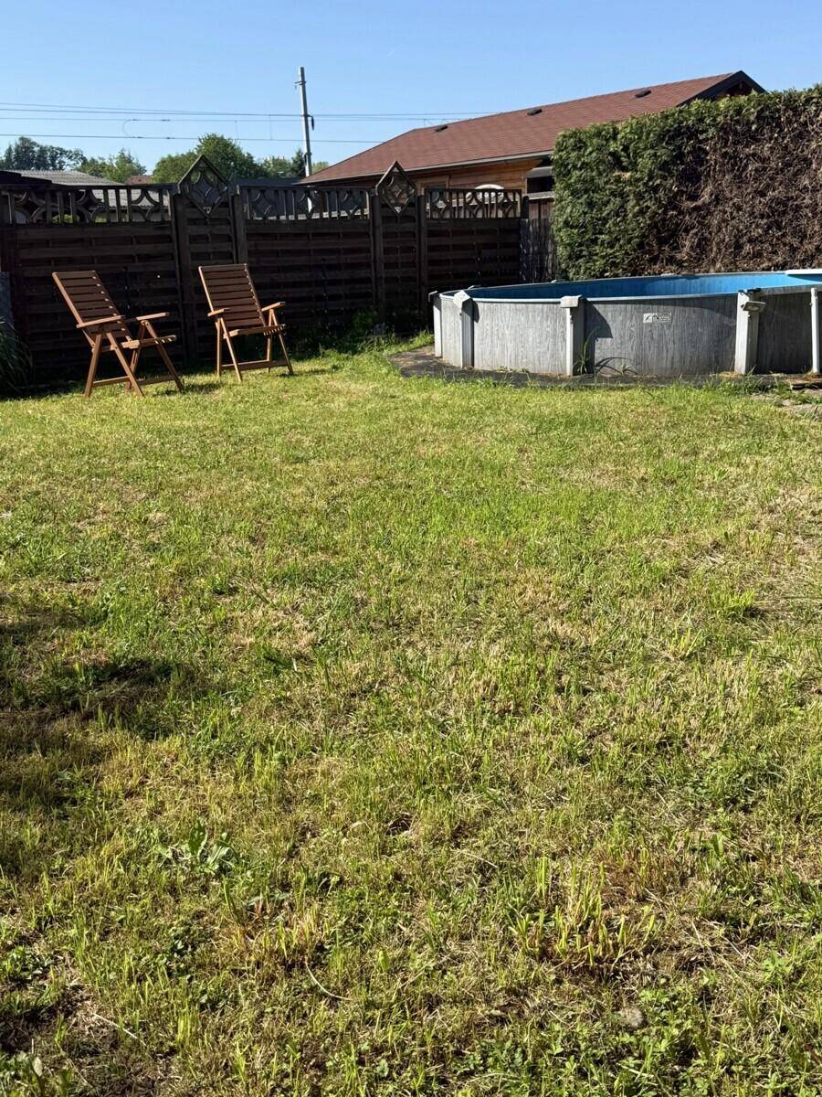 Großer Gartenbereich mit Rasenfläche, einem Aufstellpool und Holzliegestühlen unter blauem Himmel.