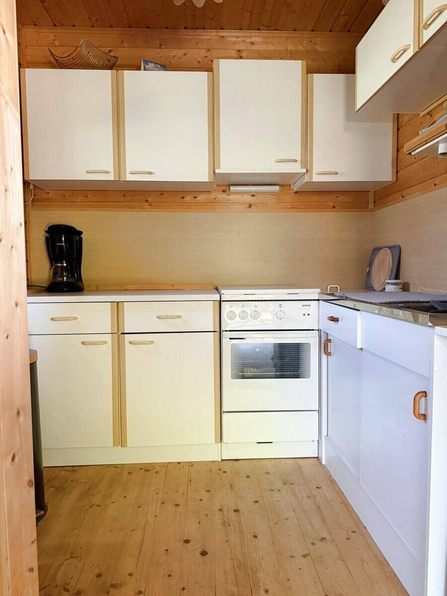 Funktionale Küche mit weißen Unterschränken, einem Herd und Holzvertäfelung an Wänden und Decke.