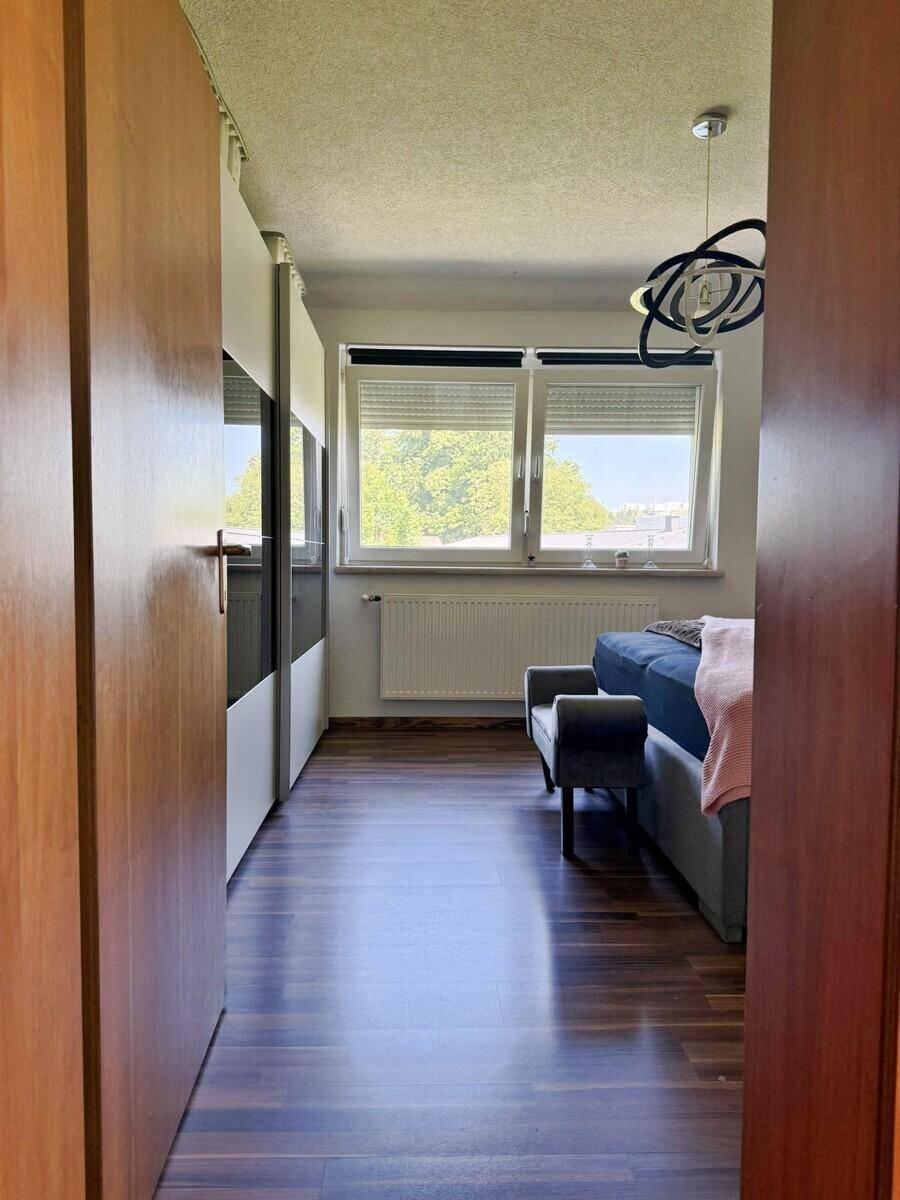 Flur führt zu einem Schlafzimmer mit großem Fenster und dunklem Laminatboden.