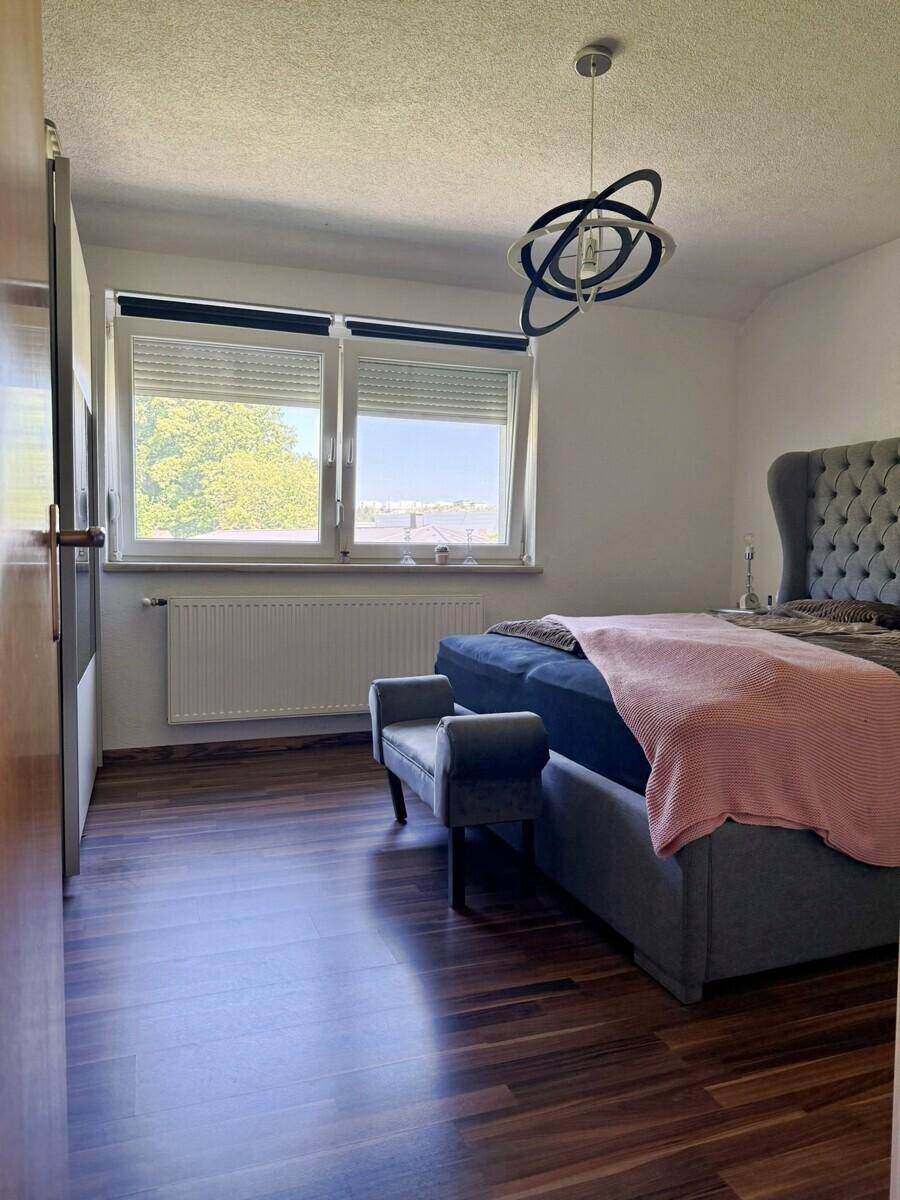 Helles Schlafzimmer mit großem Bett, Sessel und dunklem Laminatboden.