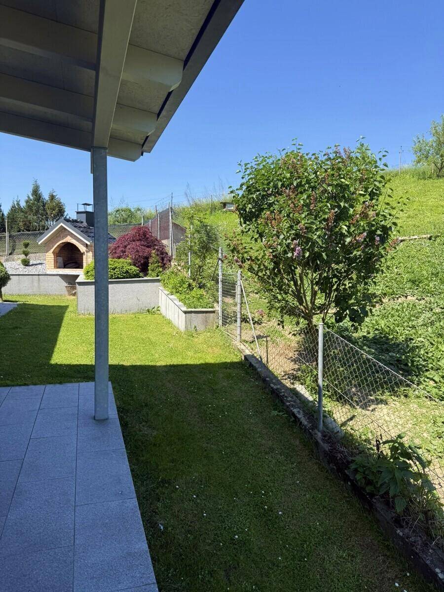 Überdachter Terrassenbereich neben dem Rasen mit Blick auf den Garten und Pizzaofen.