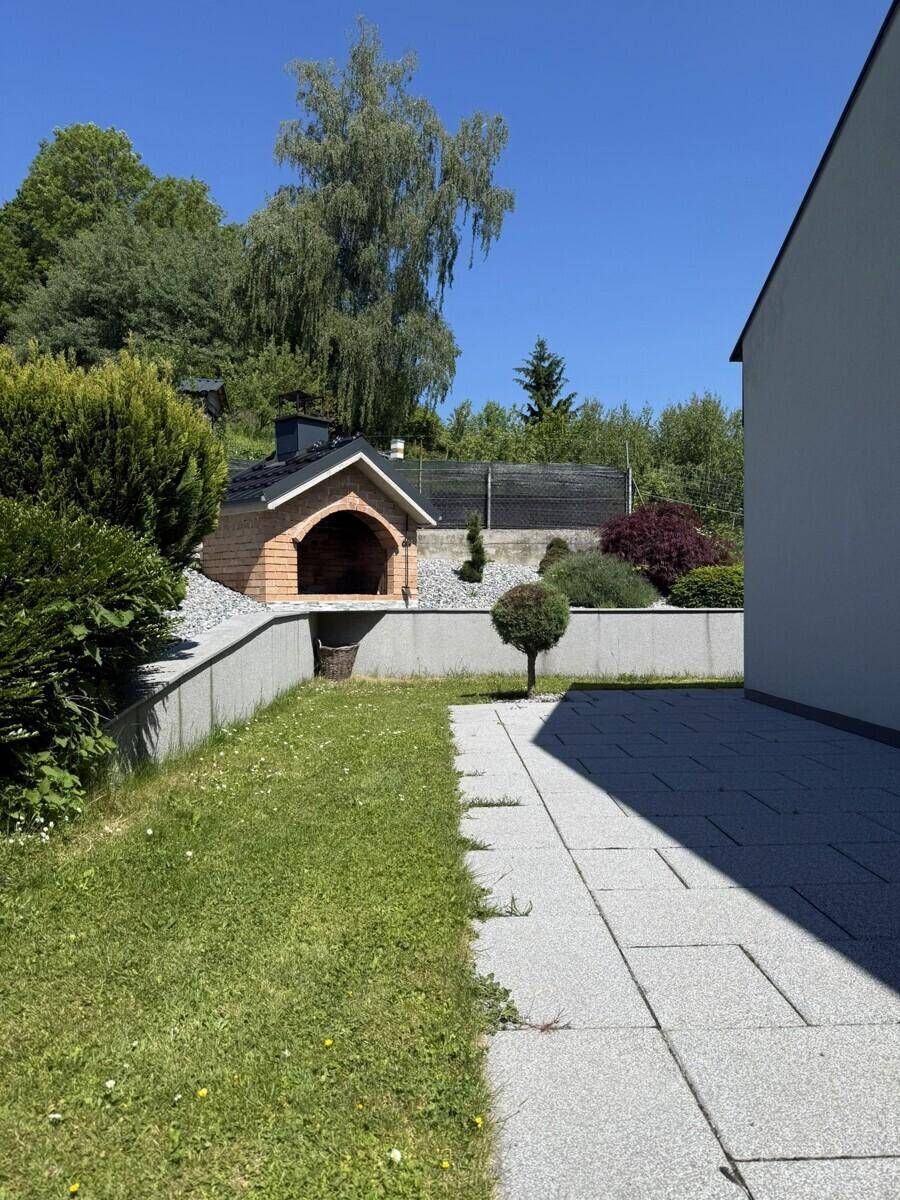 Terrasse mit Steinplatten und Rasenfläche, im Hintergrund ein gemauerter Pizzaofen.