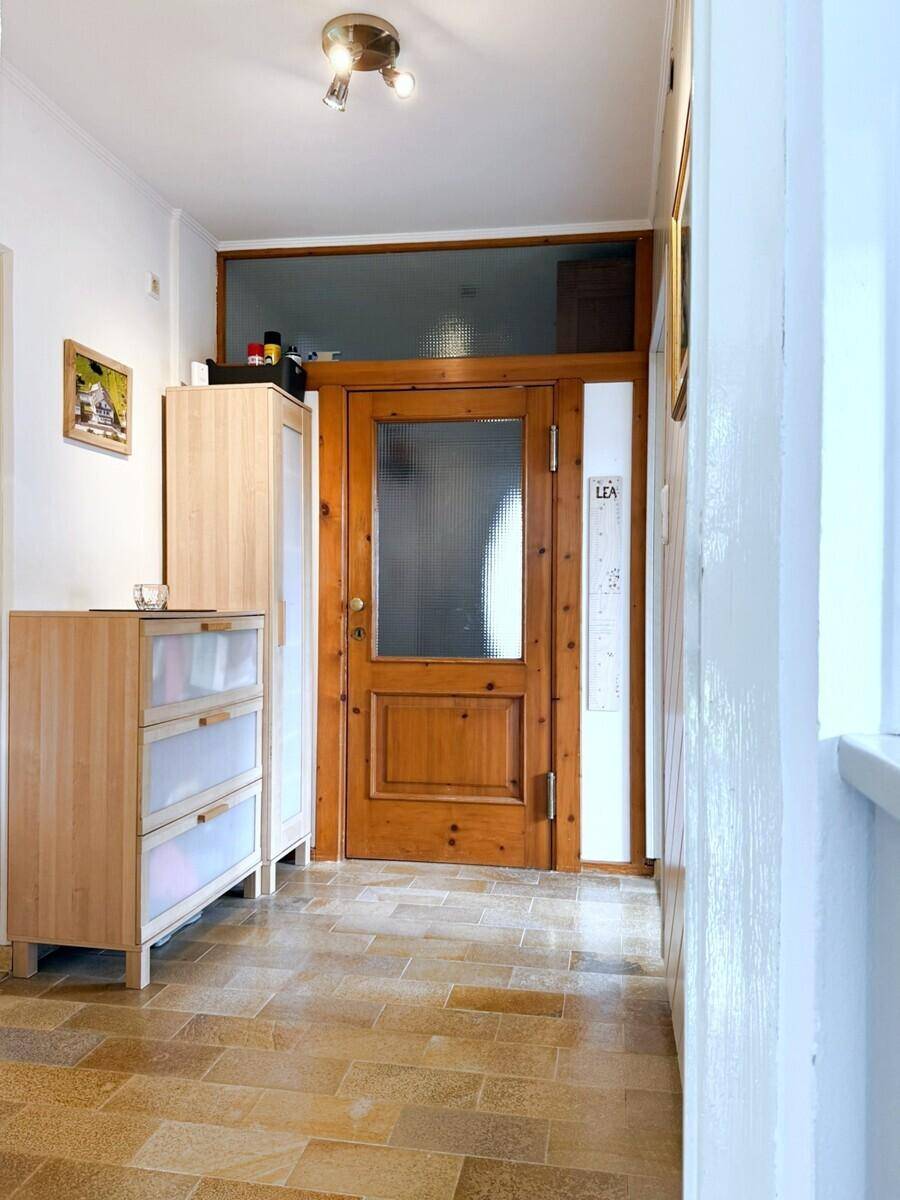 Heller Eingangsbereich mit Holztür, Fliesenboden und hellen Holzmöbeln.