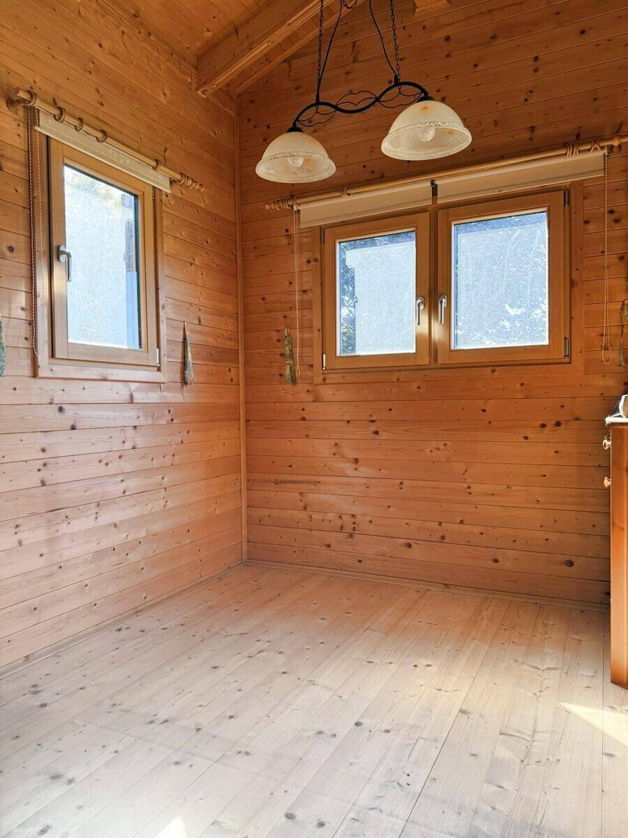 Helles Zimmer mit Holzvertäfelung an Wänden und Decke, Holzboden und zwei Fenstern.