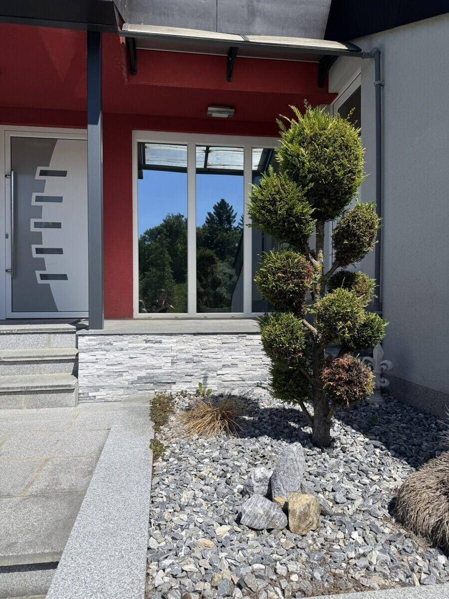 Eingangsbereich des Hauses mit moderner Tür, großem Fenster und dekorativem Kiesbeet.