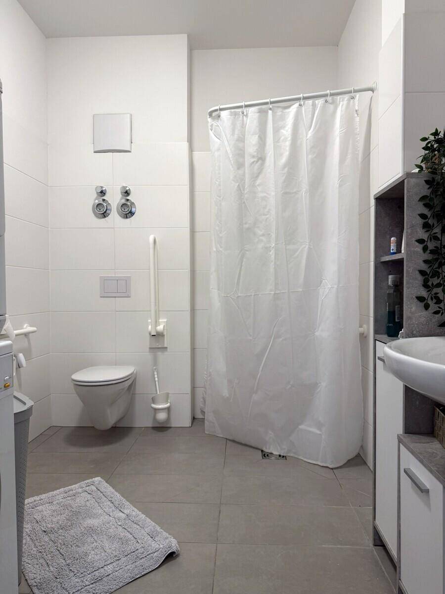 Helles Badezimmer mit Dusche, WC und Fliesenboden in neutralen Farben.