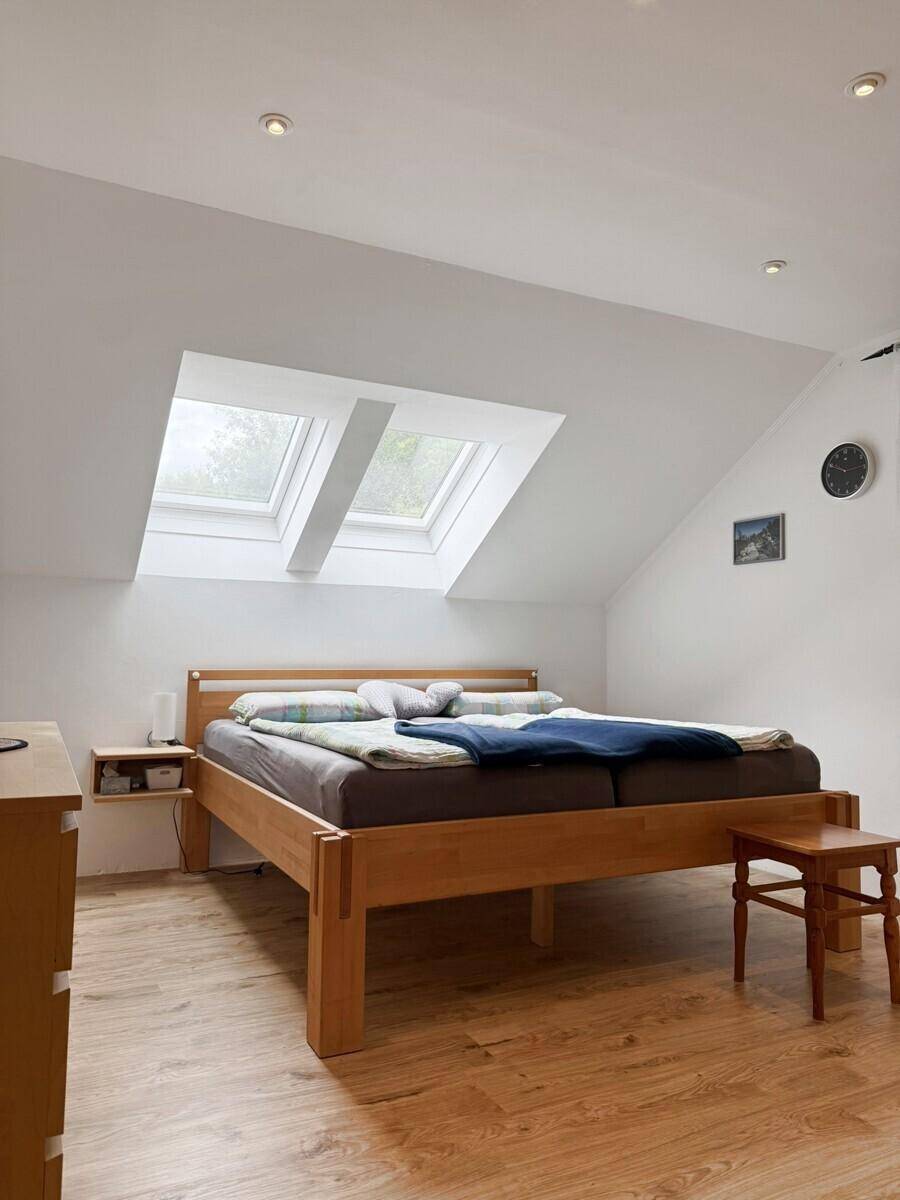 Schlafzimmer im Dachgeschoss mit Holzbett, Holzboden und zwei Dachfenstern für viel Licht.