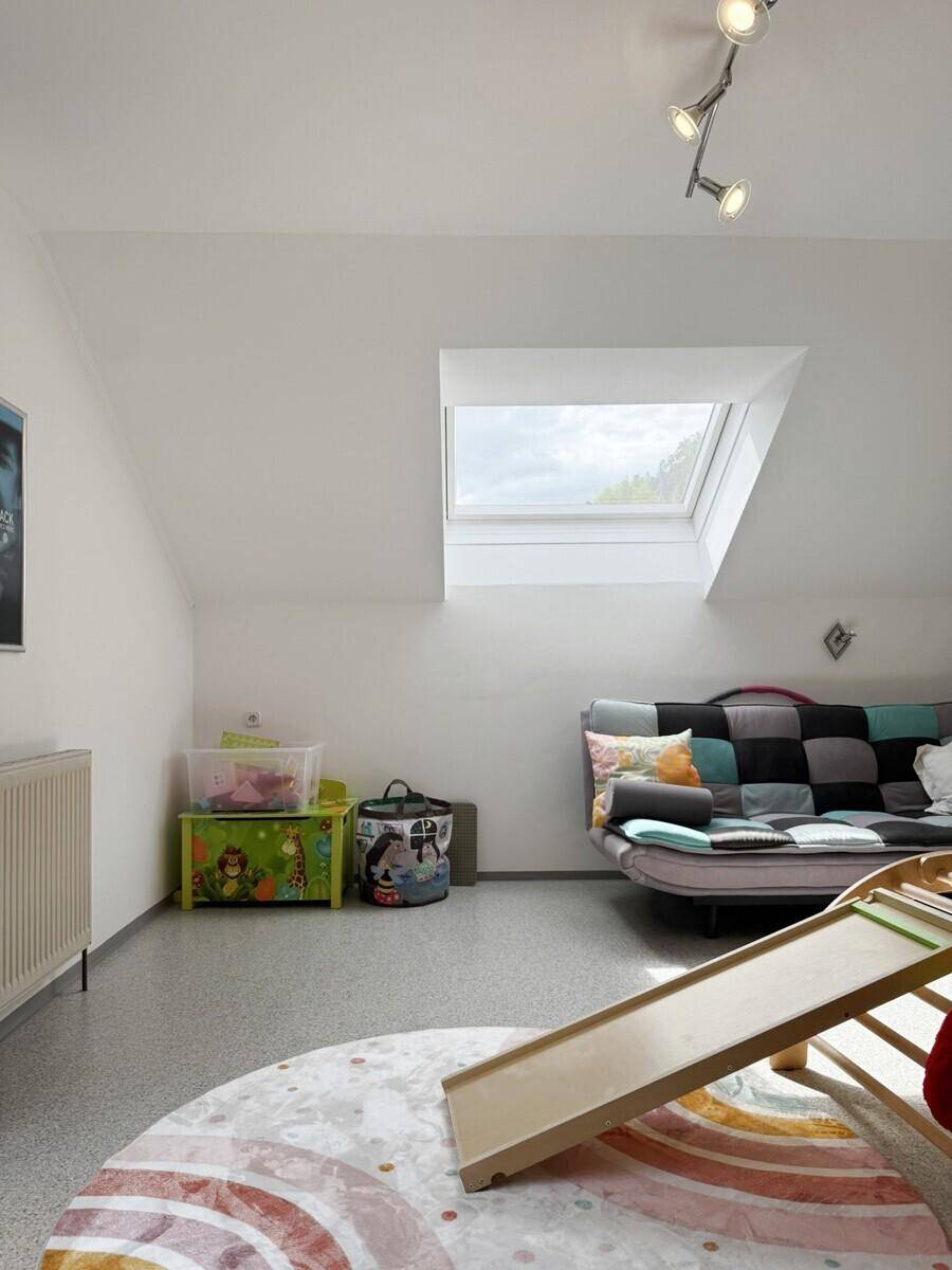 Spielzimmer im Dachgeschoss mit Dachfenster, Sofa und Spielgeräten auf hellem Boden.