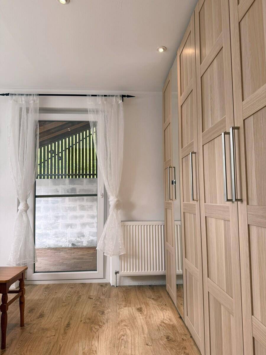 Schlafzimmer mit hellem Holzboden, großem Kleiderschrank und Zugang zu einem Außenbereich.