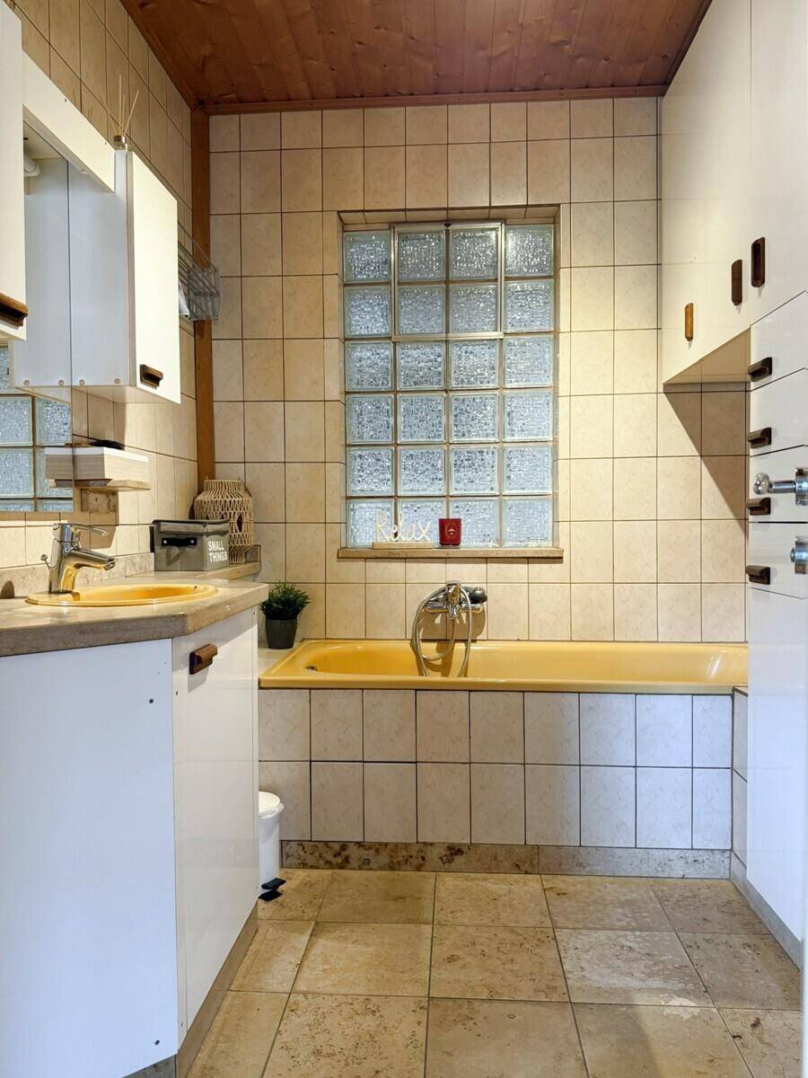 Badezimmer im 80er-Jahre-Stil mit gelber Badewanne, Fliesen und Holzdecke.