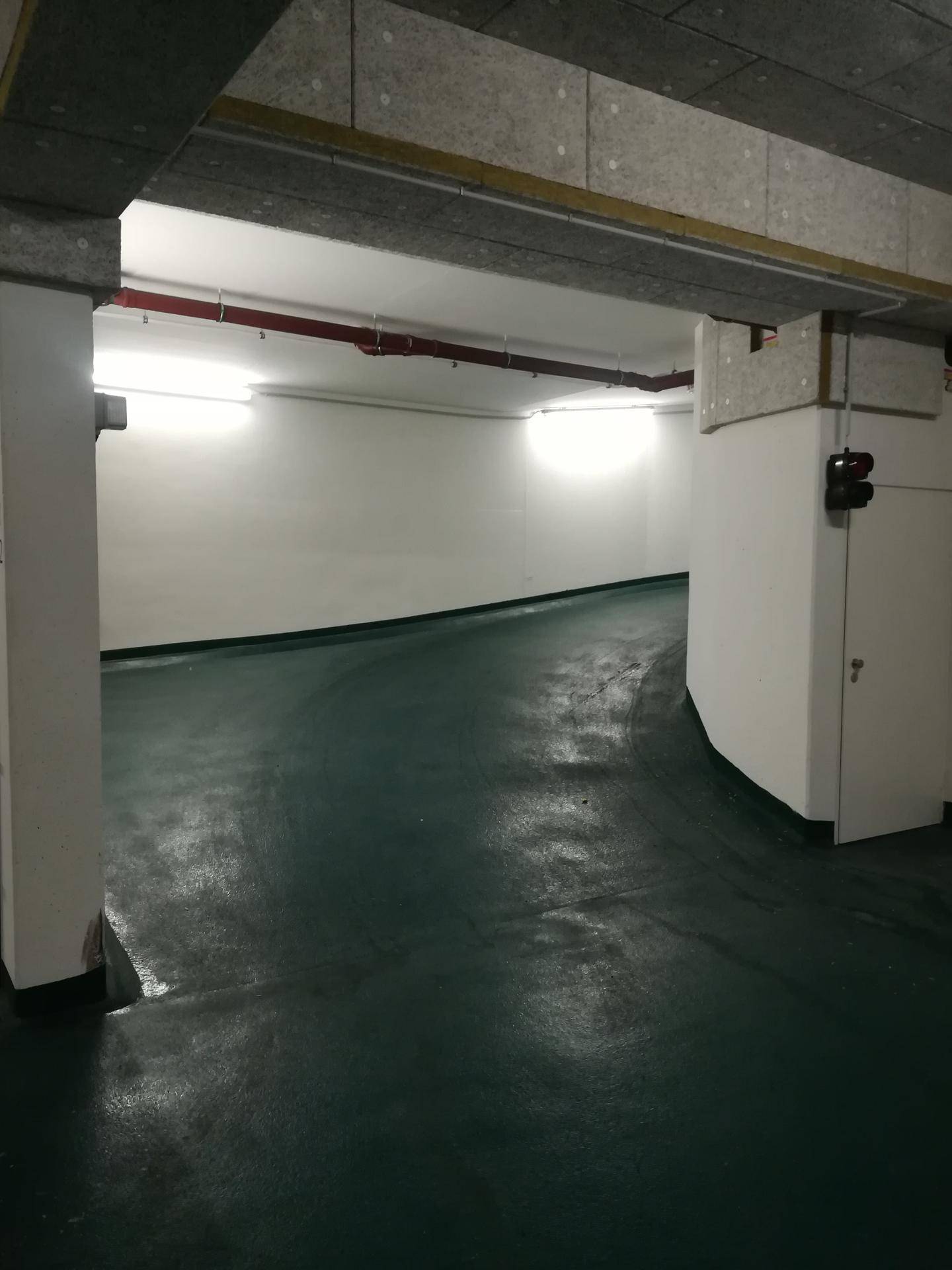Zufahrtsrampe in einer Tiefgarage mit dunkelgrünem Boden und weiß gestrichenen Wänden.