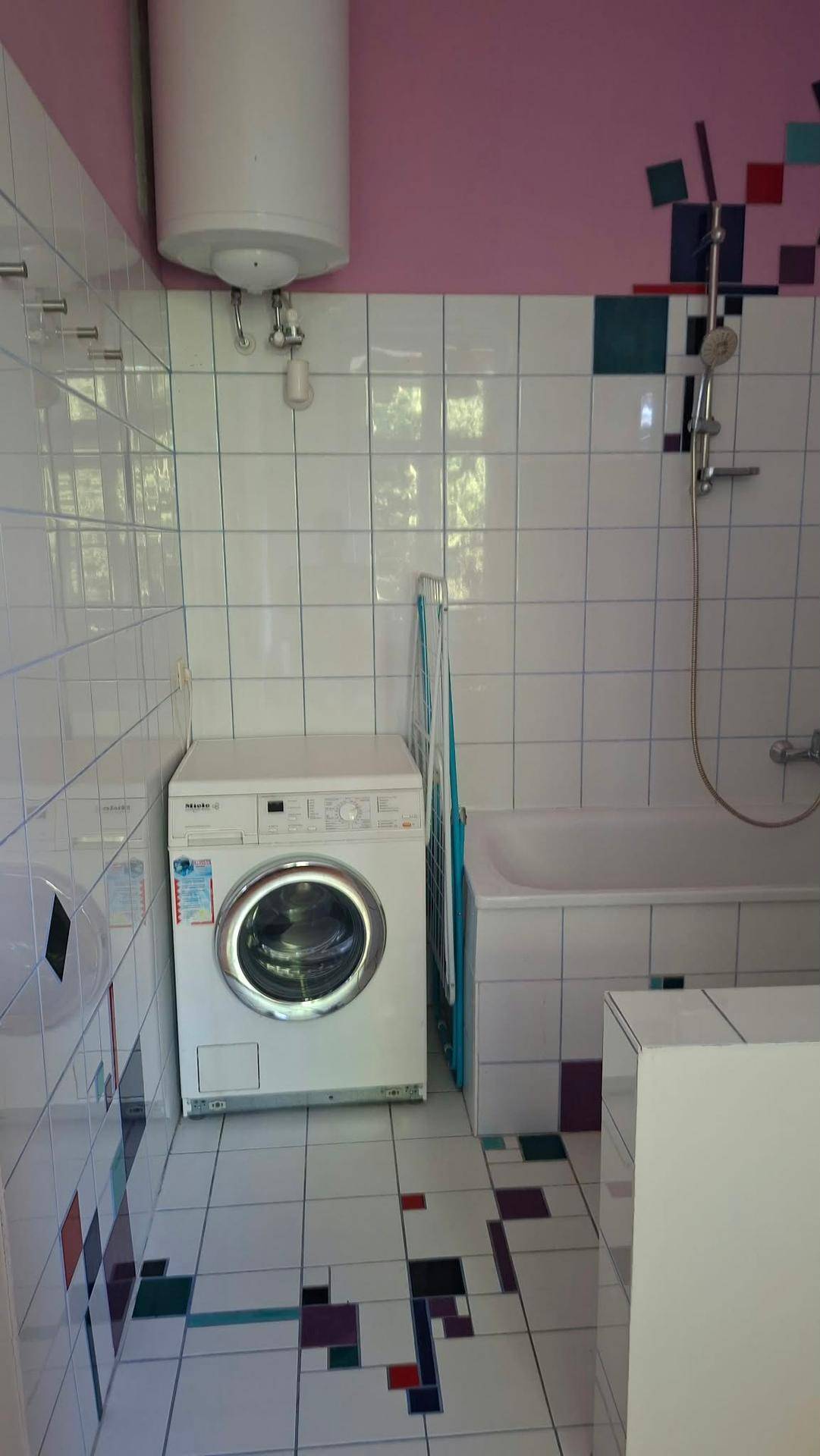 Badezimmer mit weißen Fliesen, Badewanne, Dusche und Waschmaschine, mit farbigen Akzenten.