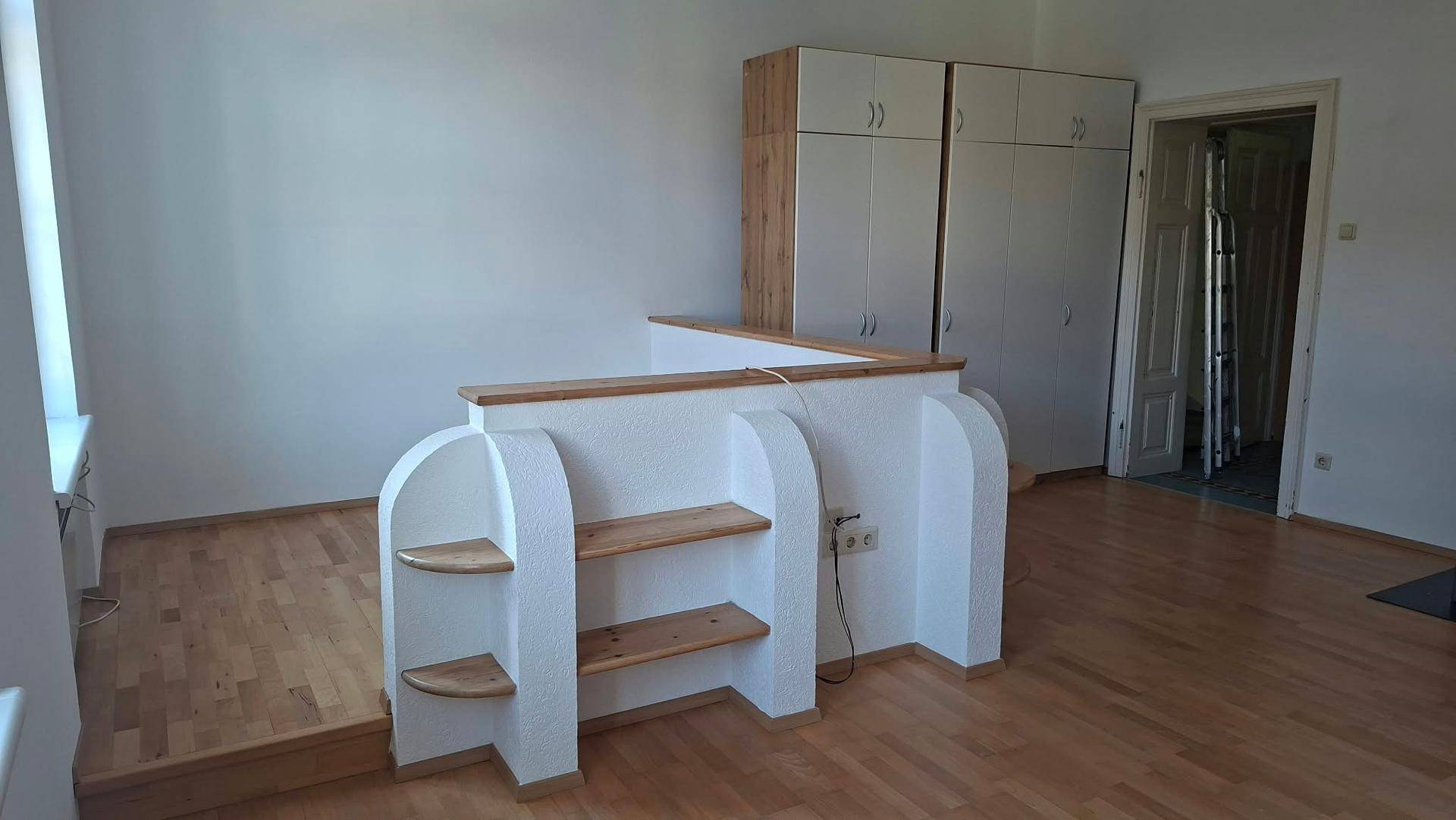 Geräumiges Wohnzimmer mit Holzboden, weißen Wänden und praktischen Einbauschränken.