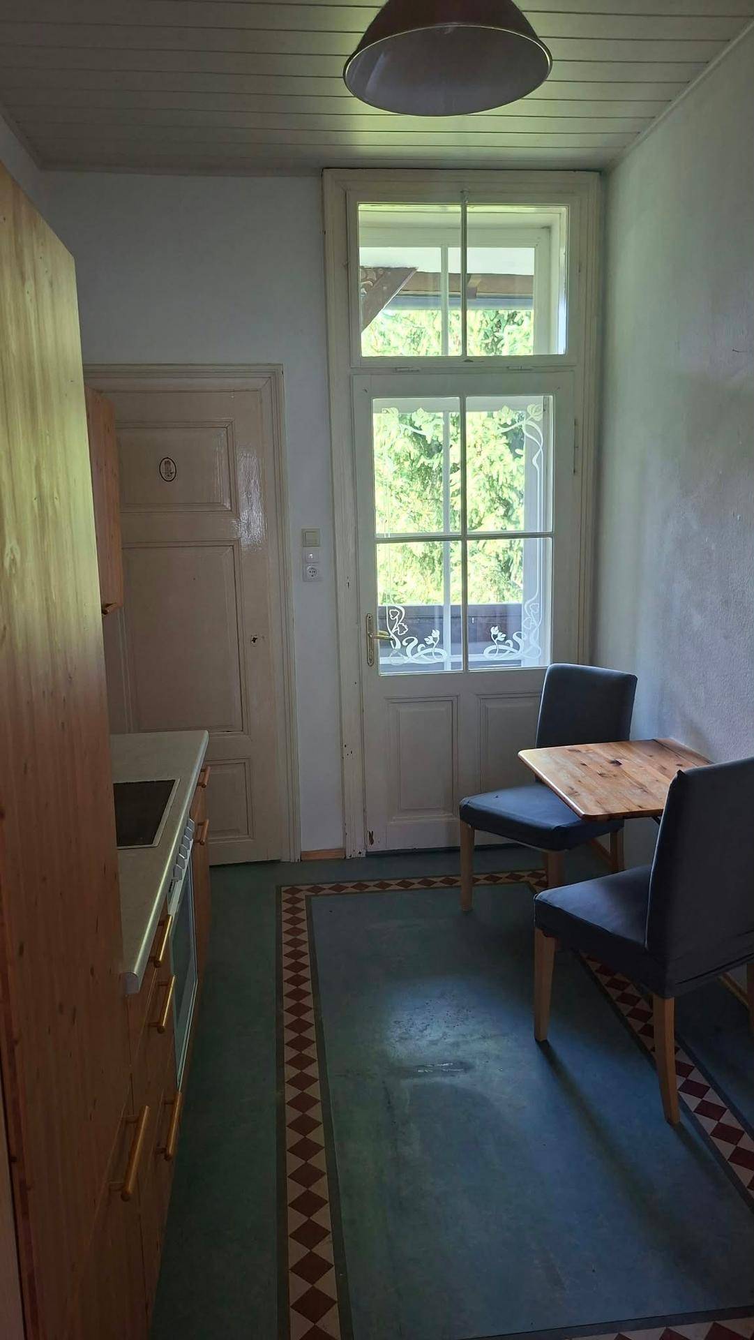 Gemütlicher Essbereich in der Küche mit Holztisch, zwei Stühlen und Blick ins Grüne durch das Fenster.