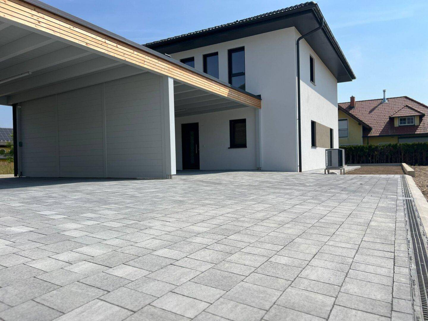 Modernes Einfamilienhaus mit Carport und gepflasterter Auffahrt an einem sonnigen Tag.